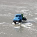 A blue toy truck navigates foamy ocean waves on Guaratuba Beach, Brazil.