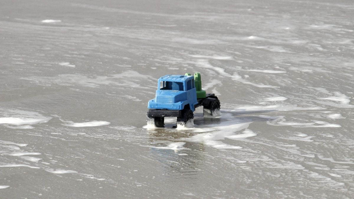 A blue toy truck navigates foamy ocean waves on Guaratuba Beach, Brazil.